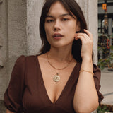 Woman in a brown dress standing against an ornate wall.