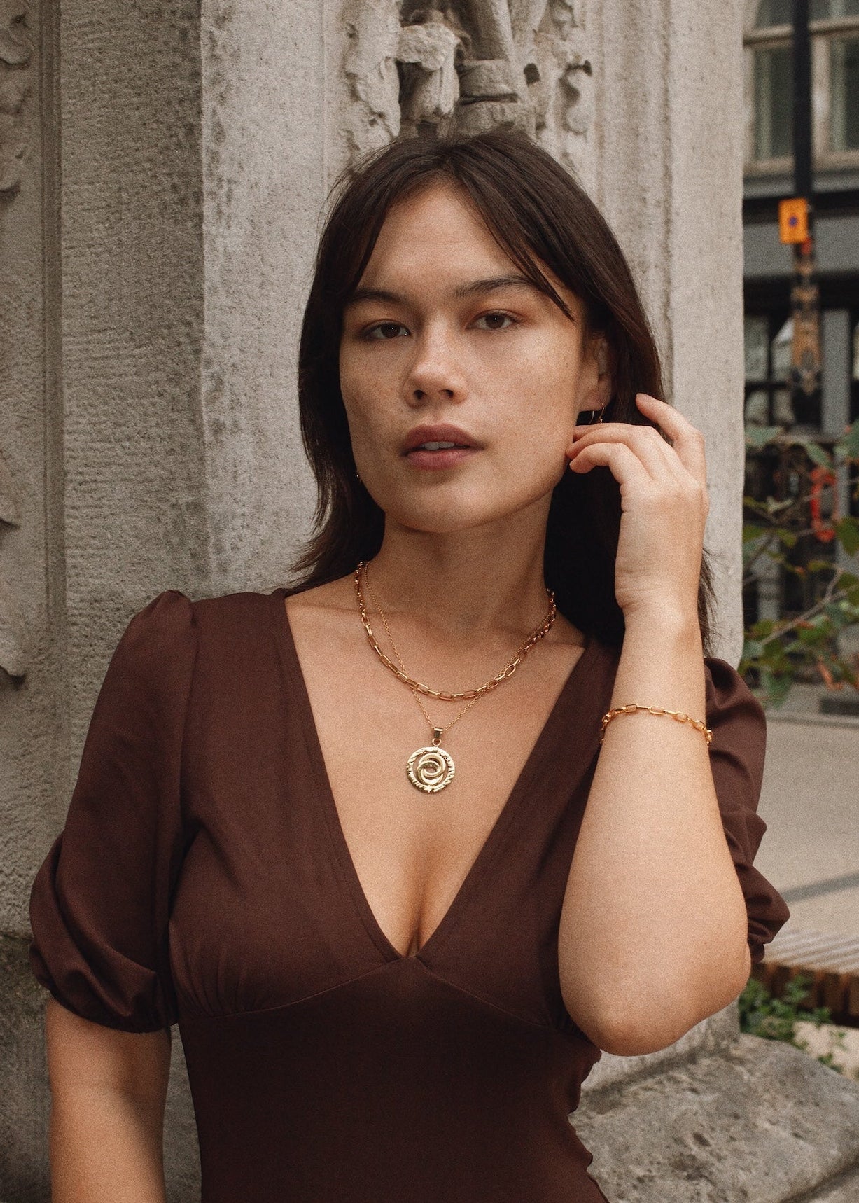 Woman in a brown dress standing against an ornate wall.