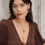 Woman wearing a brown dress with a deep neckline, standing against a textured wall.