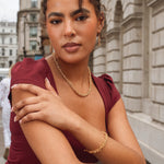 Woman in a burgundy dress with gold jewelry against an urban background