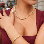 Woman wearing a gold necklace and bracelet with a blurred city street background