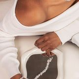 Person wearing a white sweater with a necklace and bracelet, sitting on a white chair.