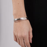 Silver bracelet on a wrist with a plain background