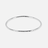 A thin, polished silver bangle bracelet with a subtle hammered or textured finish, shown against a solid light gray background.