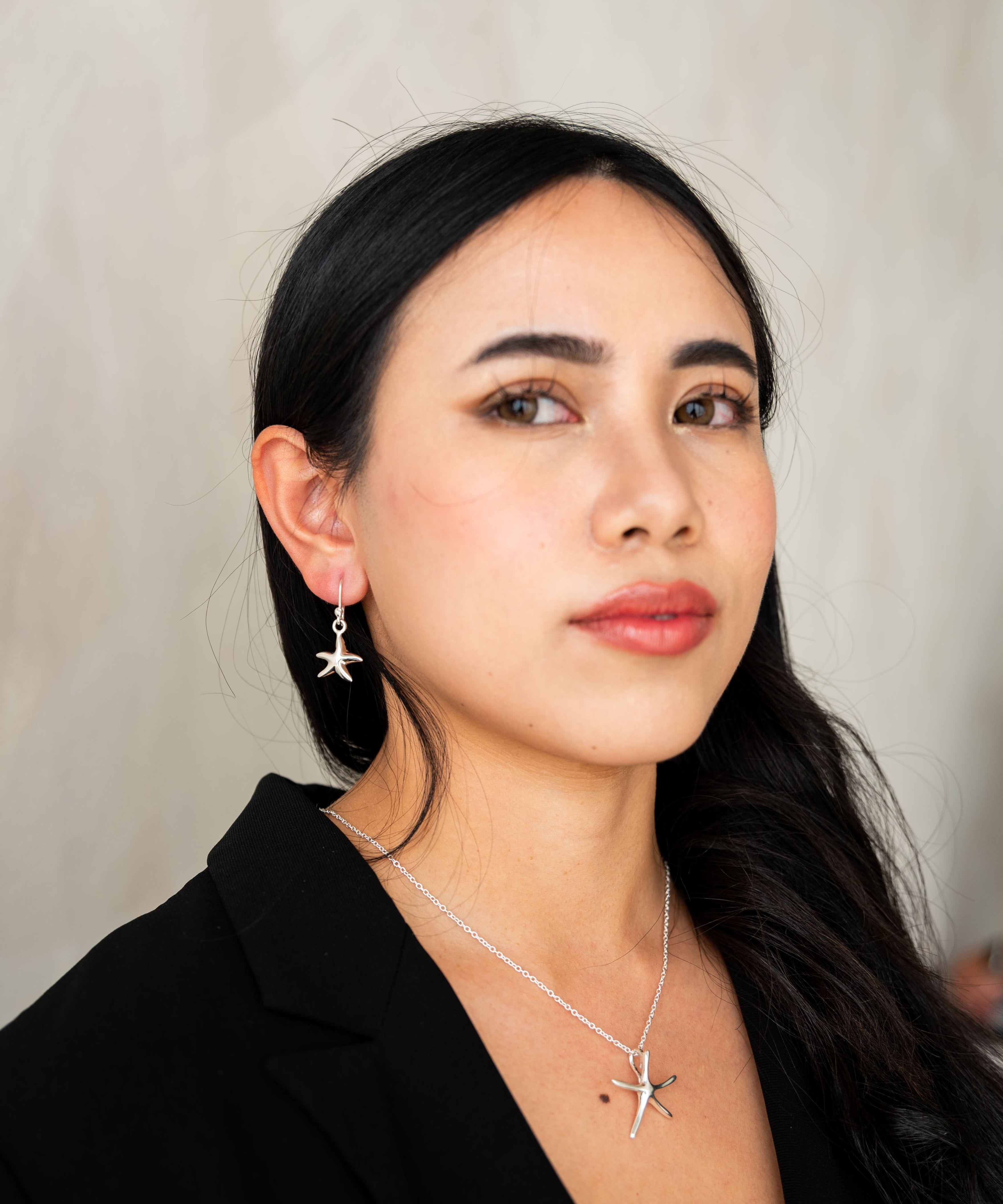 Woman wearing star-shaped earrings and a necklace against a neutral background