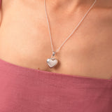 Silver heart-shaped pendant necklace on a person wearing a pink top.