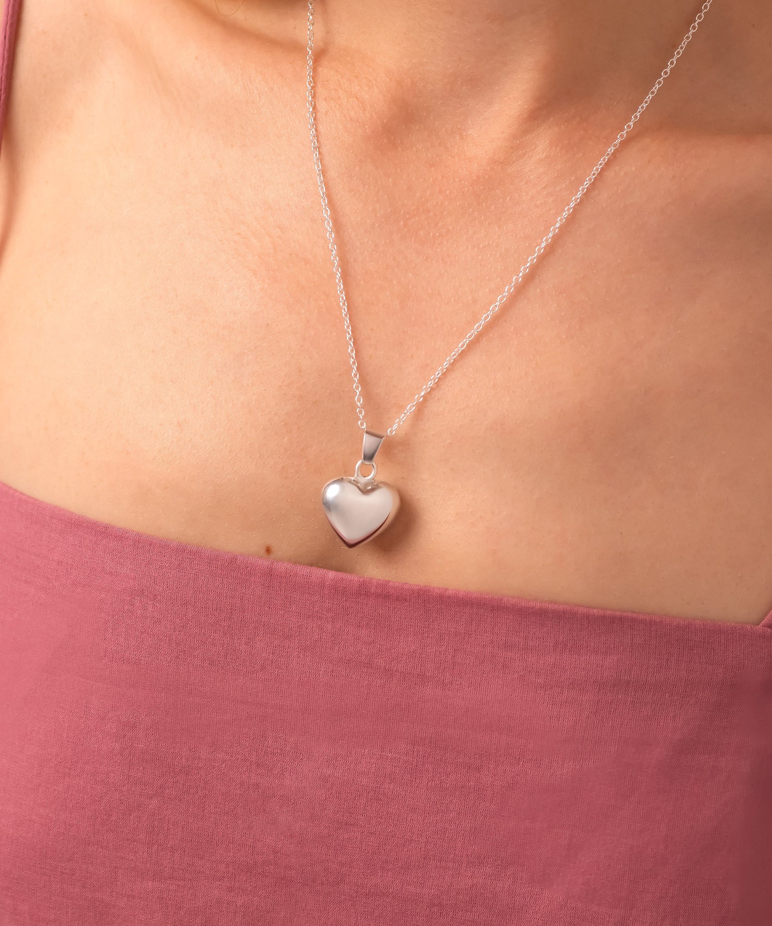 Silver heart-shaped pendant necklace on a person wearing a pink top.