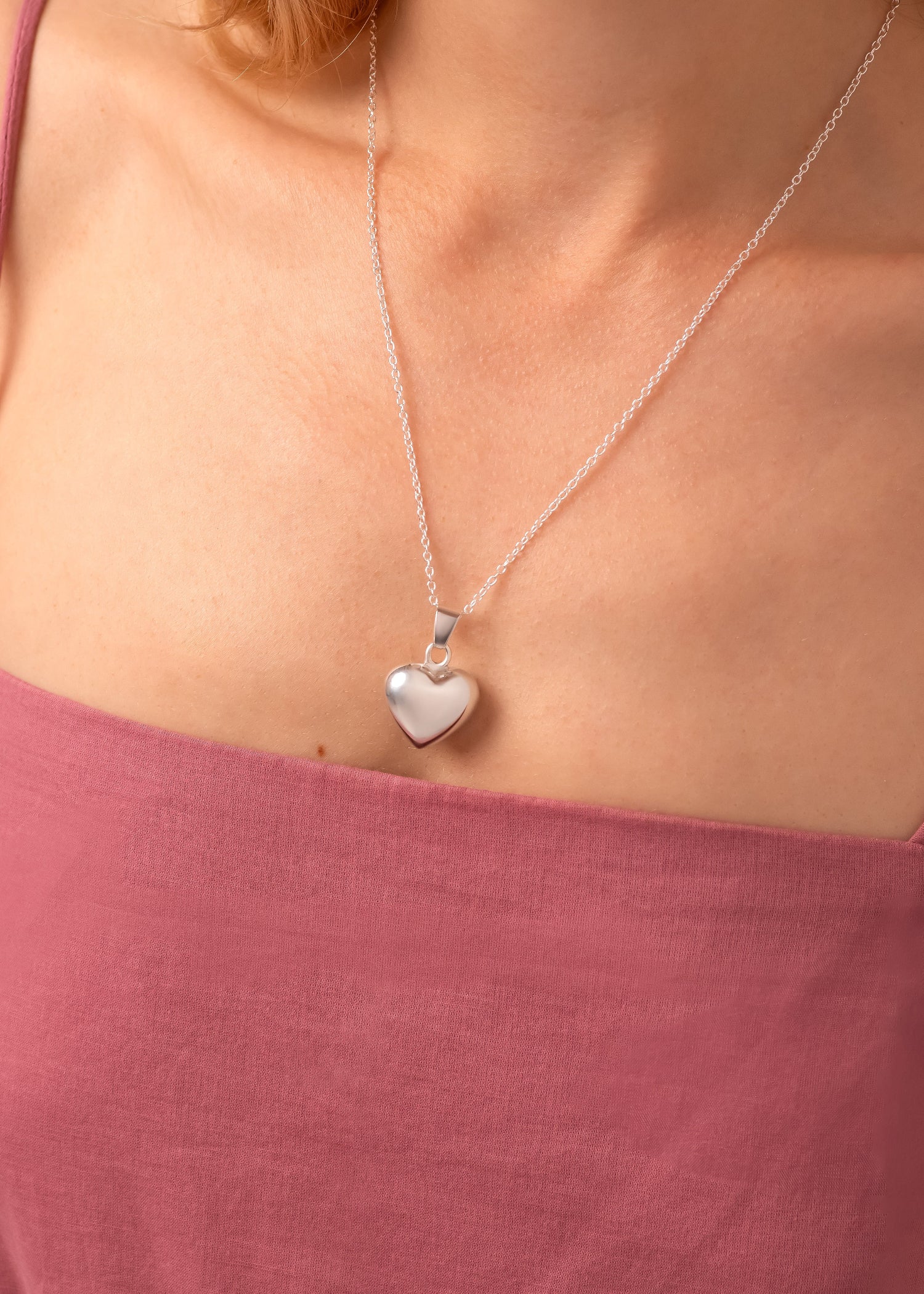 Silver heart-shaped pendant necklace on a person wearing a pink top.