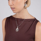 Woman wearing a necklace with a circular pendant on a plain background