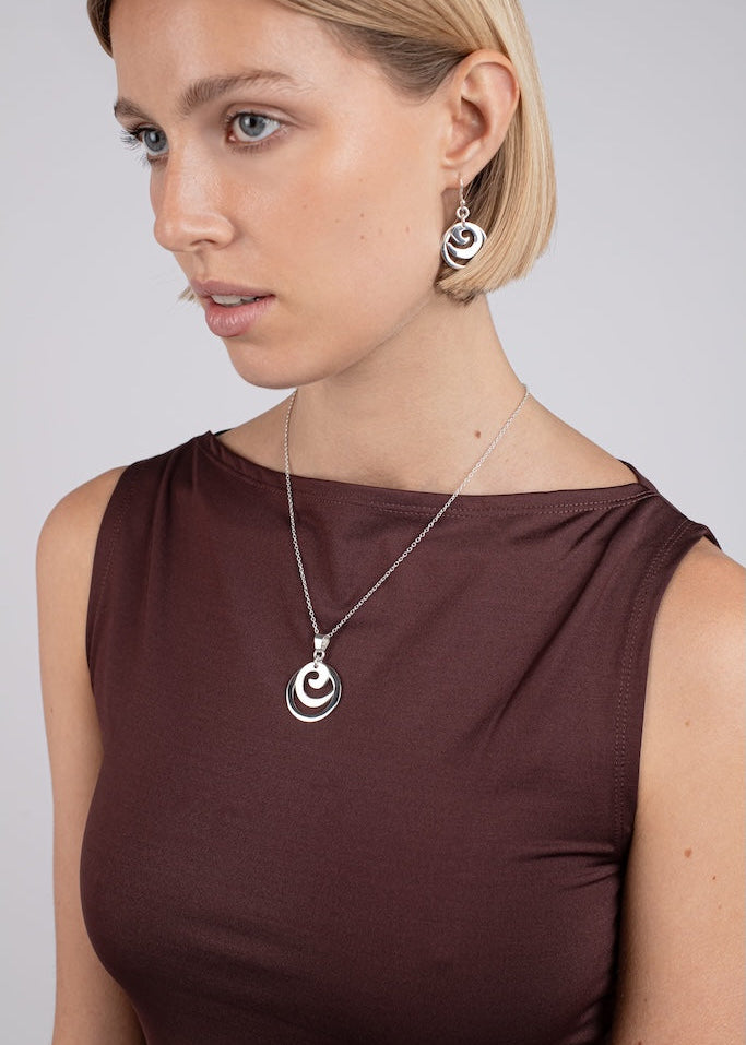 Woman wearing a necklace with a circular pendant on a plain background