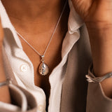 Close-up of a person wearing a silver necklace with a teardrop pendant.