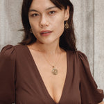 Woman wearing a brown dress with a deep neckline, standing against a textured wall.