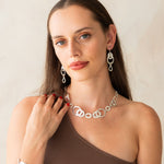 Woman wearing silver jewelry including a necklace, earrings, and bracelet against a plain background