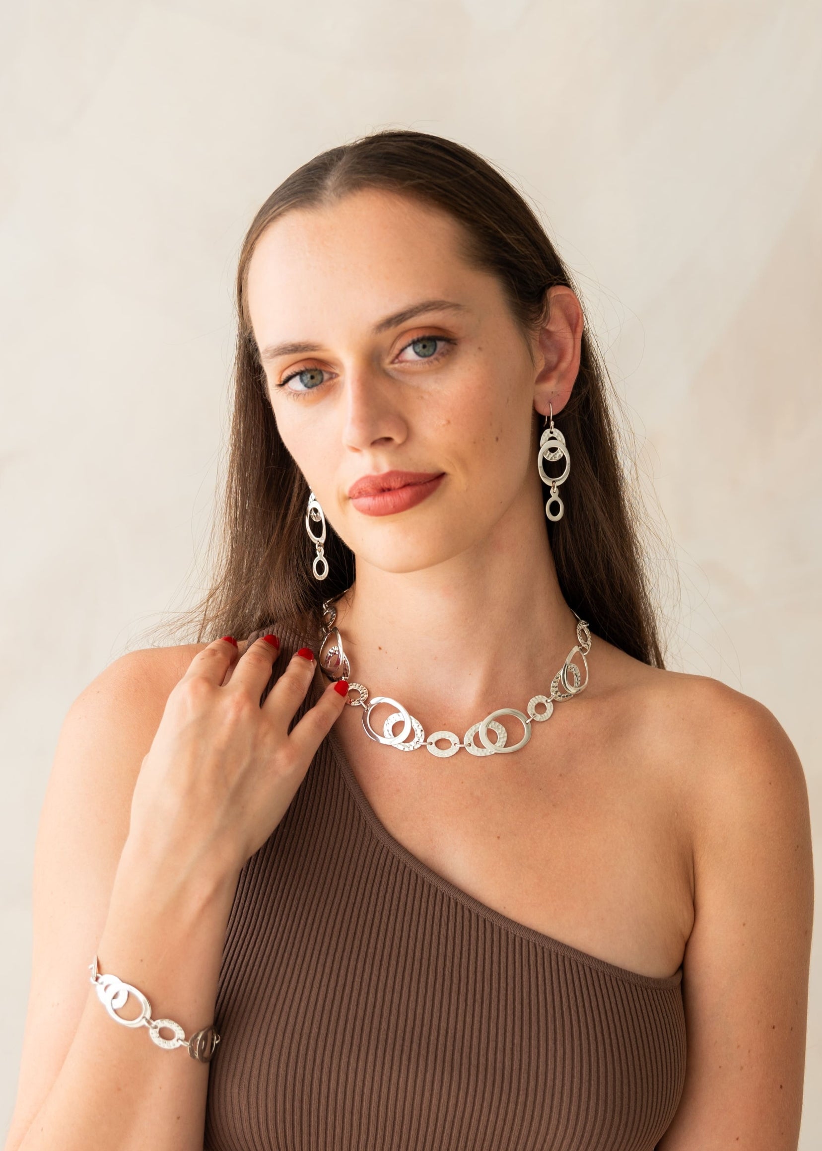 Woman wearing silver jewelry including a necklace, earrings, and bracelet against a plain background