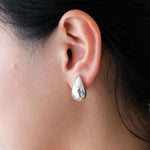Close-up of an ear wearing a silver teardrop earring with dark hair and blurred background