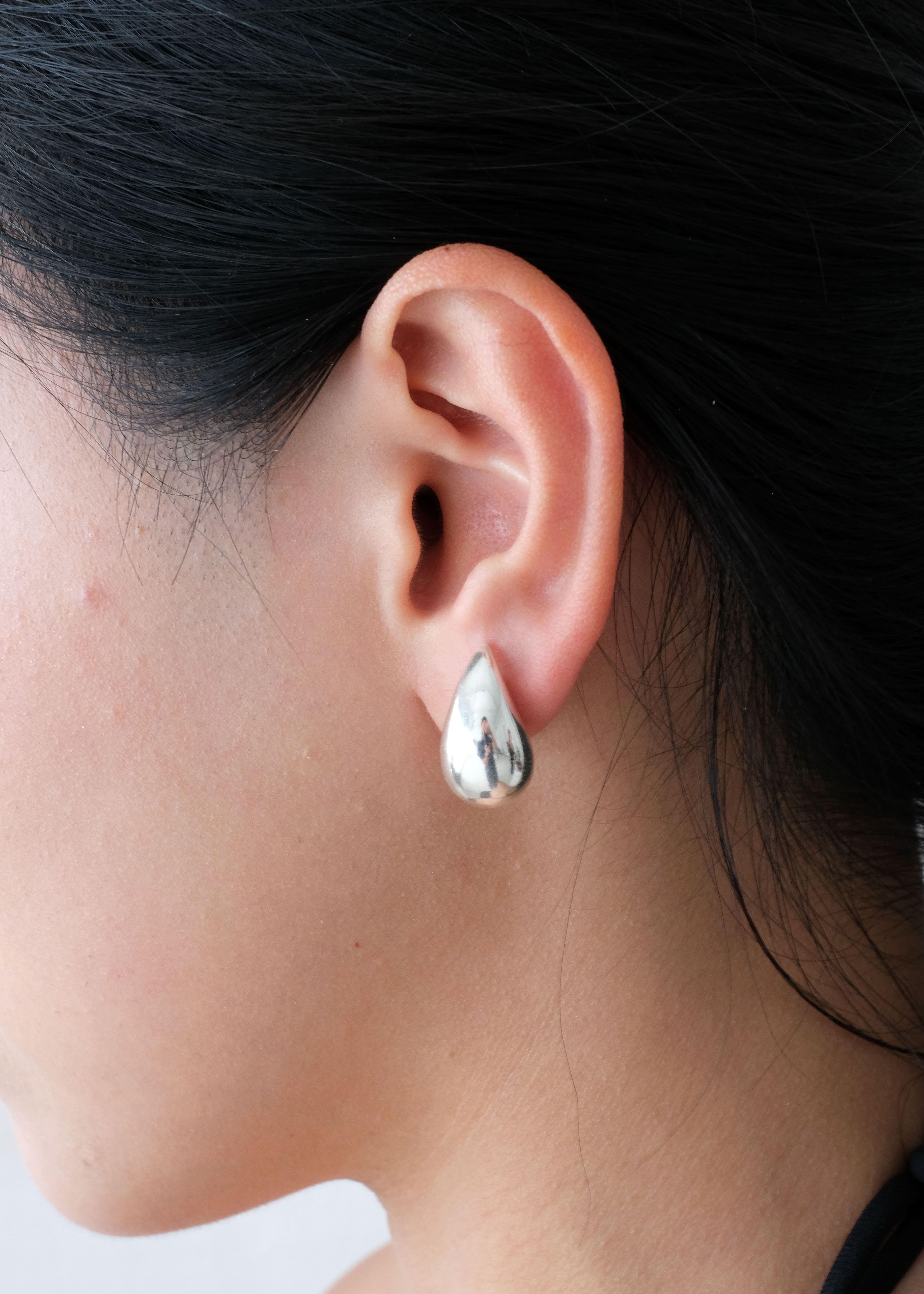 Close-up of an ear wearing a silver teardrop earring with dark hair and blurred background
