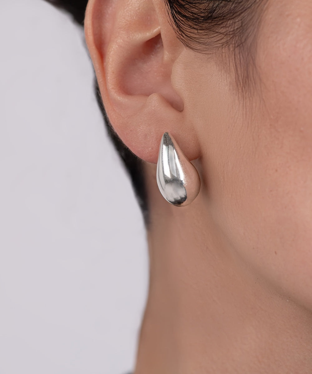 Close-up of a person wearing a silver teardrop earring with a blurred background