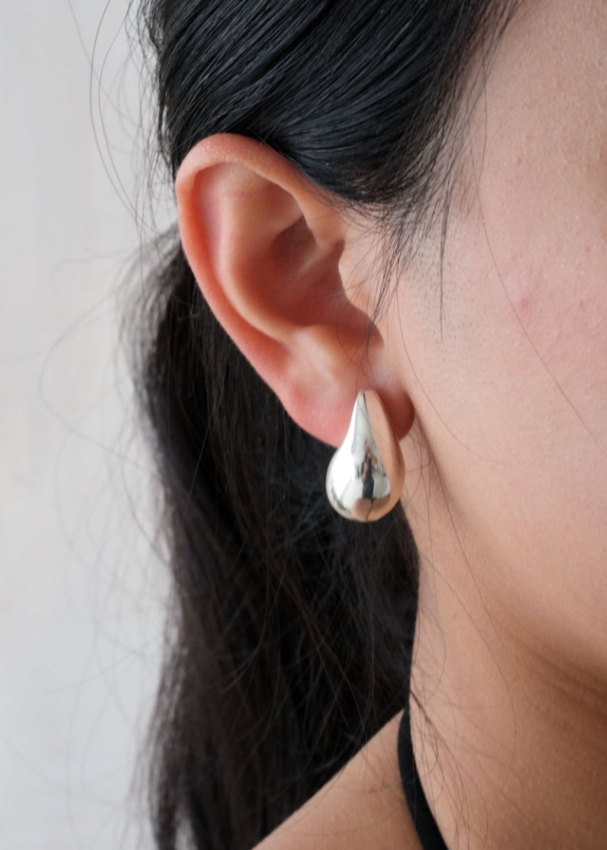 Close-up of an ear wearing a silver teardrop earring against a neutral background