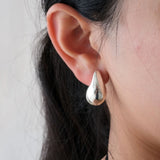 Close-up of an ear wearing a silver teardrop earring against a neutral background