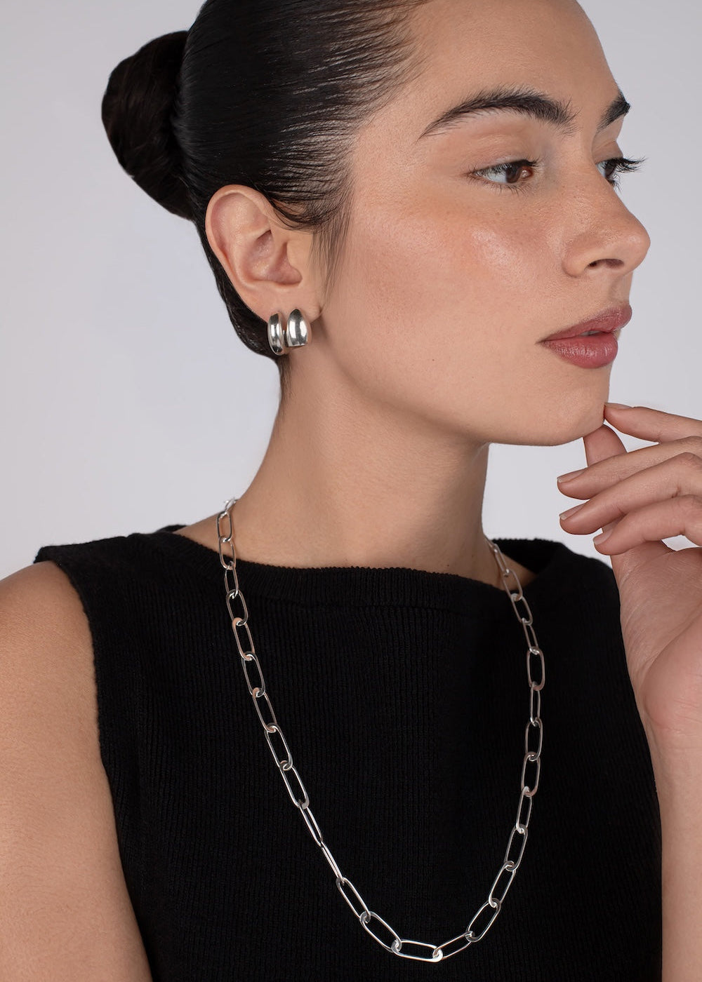 Woman wearing a silver chain necklace and earrings against a plain background