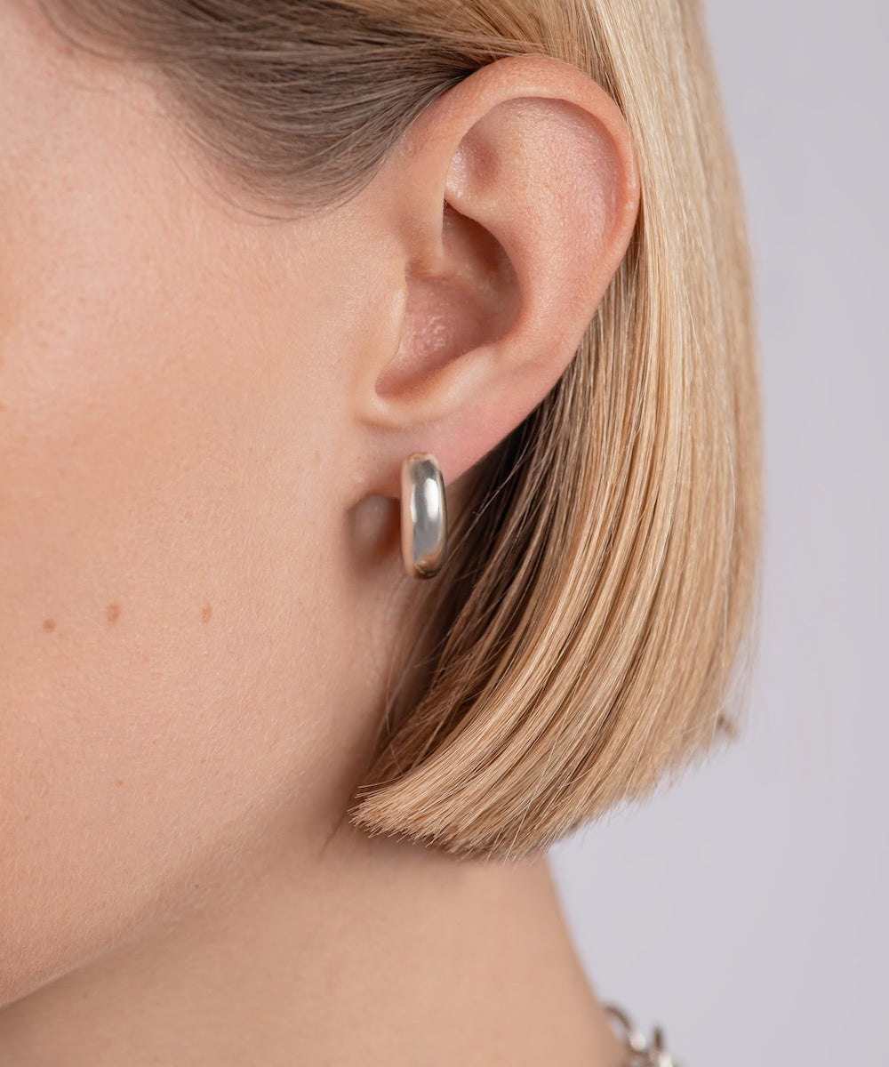 Close-up of a person wearing a silver hoop earring with a plain background