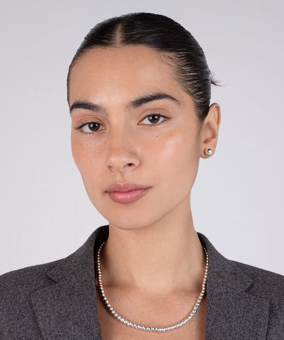 Woman wearing a gray blazer and silver necklace against a plain background