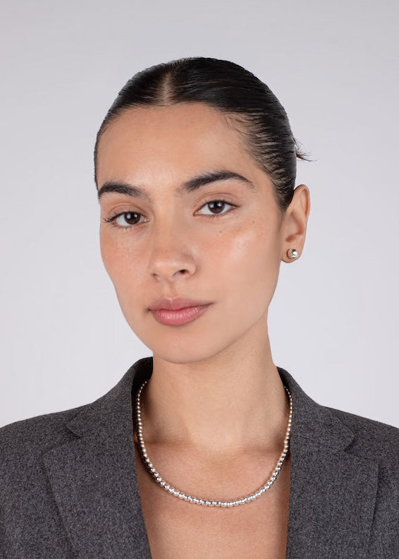 Woman wearing a gray blazer and silver necklace against a plain background