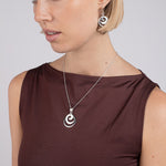 Woman wearing a brown top with a silver necklace and earrings on a plain background