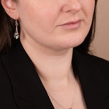 Close-up of a woman wearing a black blazer and silver earrings with a neutral background