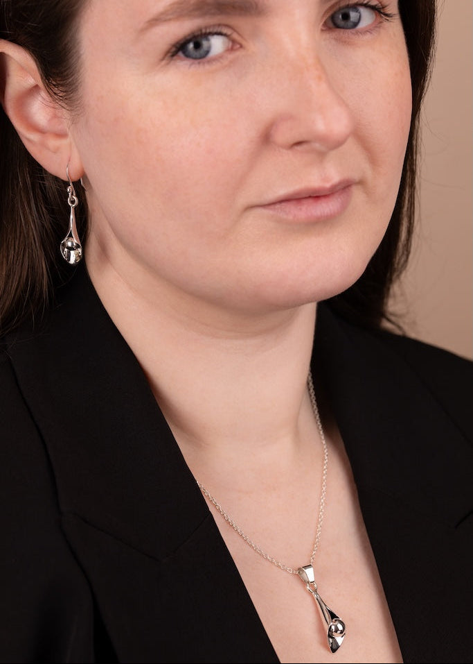 Close-up of a woman wearing a black blazer and silver earrings with a neutral background