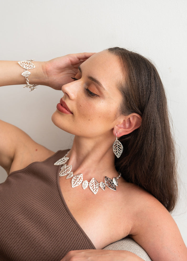 Woman wearing jewelry including earrings and a necklace against a plain background