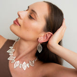 Woman wearing a silver leaf necklace and earrings against a plain background