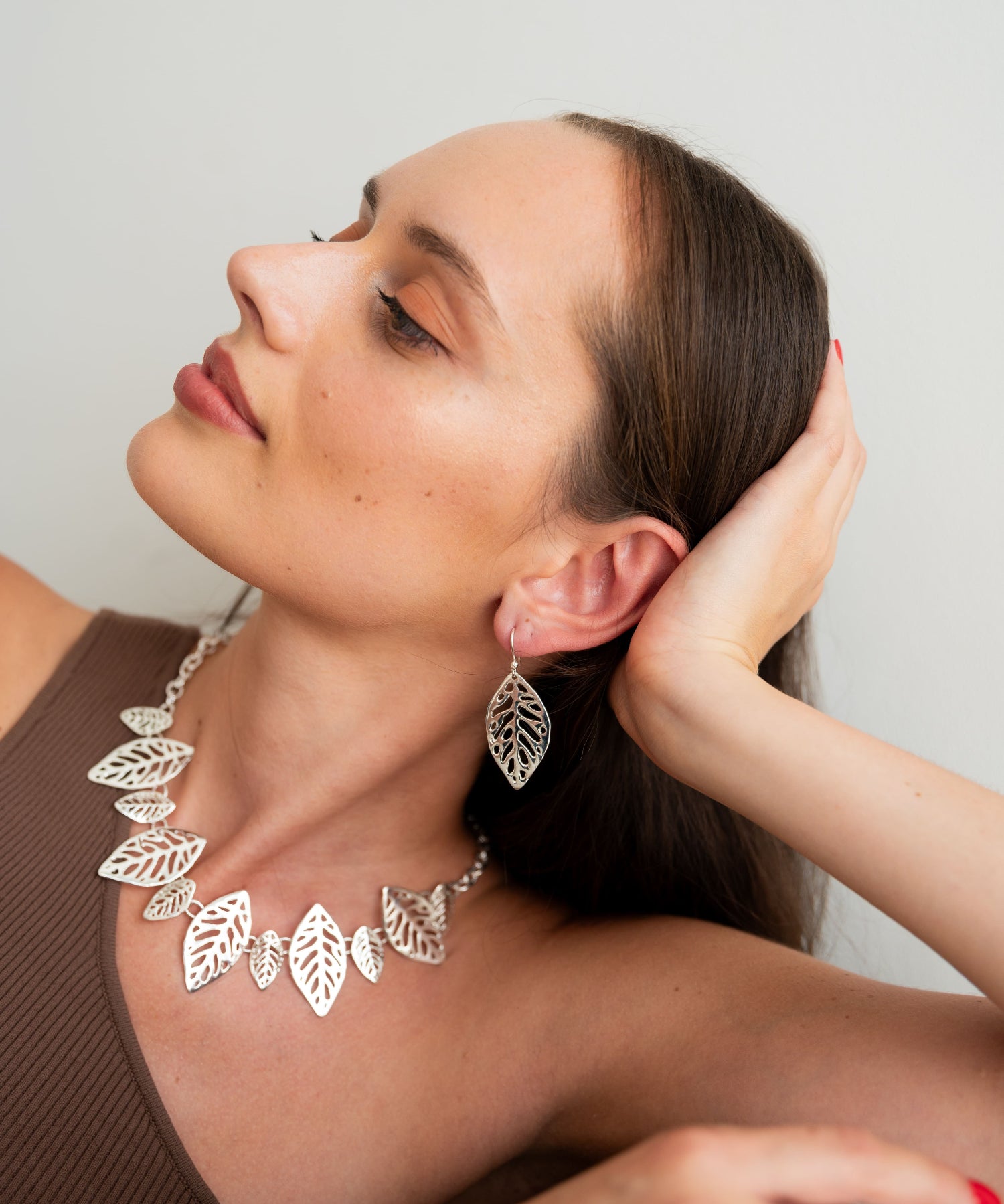 Woman wearing a silver leaf necklace and earrings against a plain background