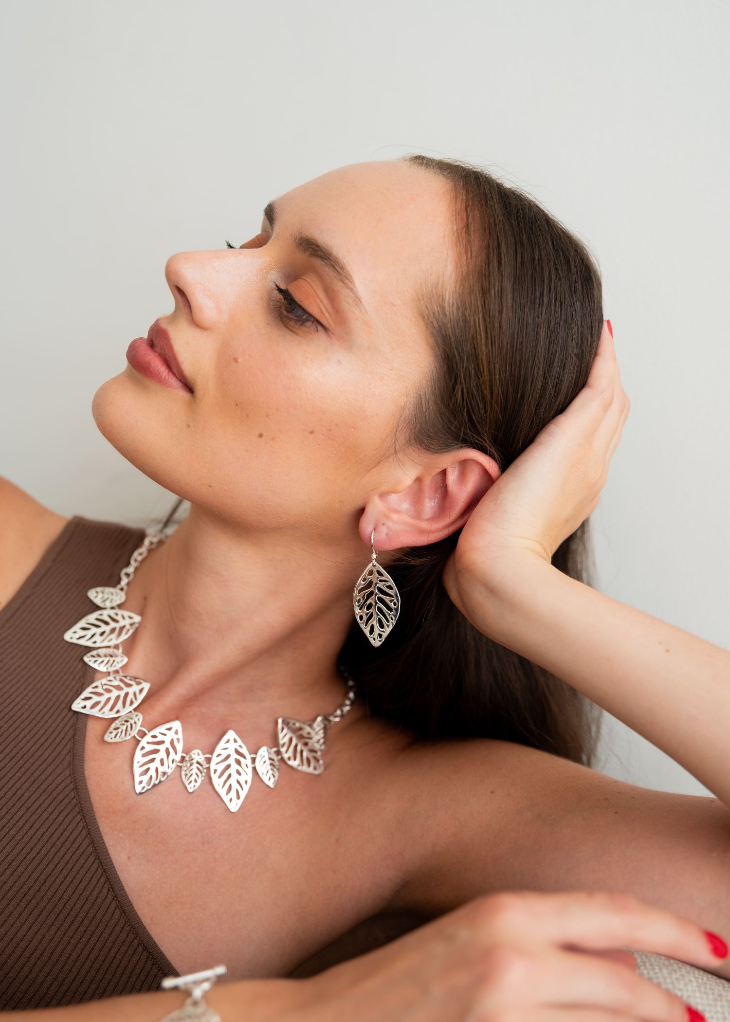 Woman wearing a silver leaf necklace and earrings against a plain background
