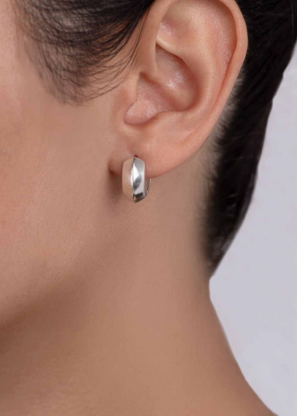 Silver hoop earring worn by a person with a neutral background