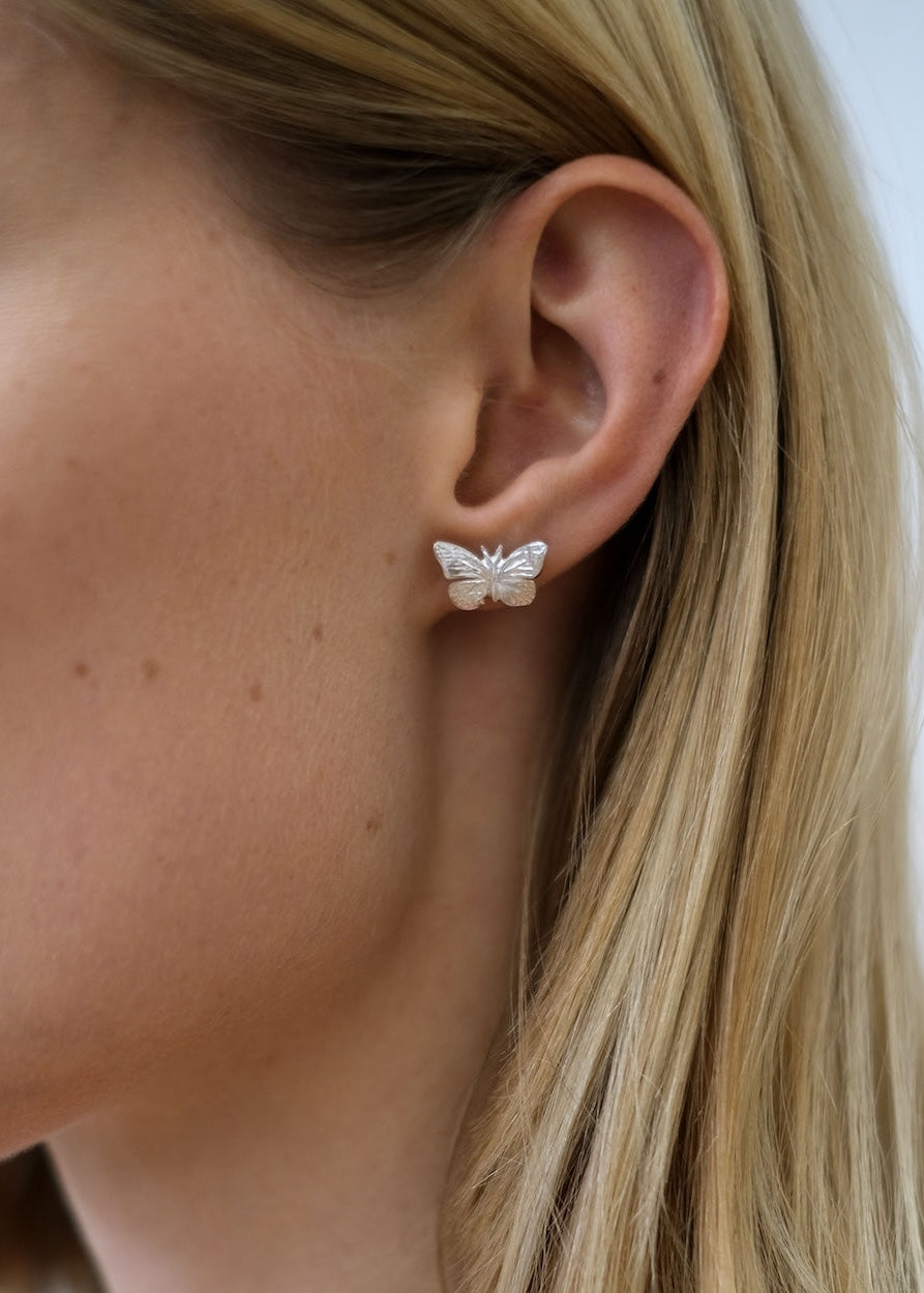 Butterfly-shaped earring worn by a person with blonde hair.
