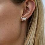 Butterfly-shaped earring worn by a person with blonde hair.