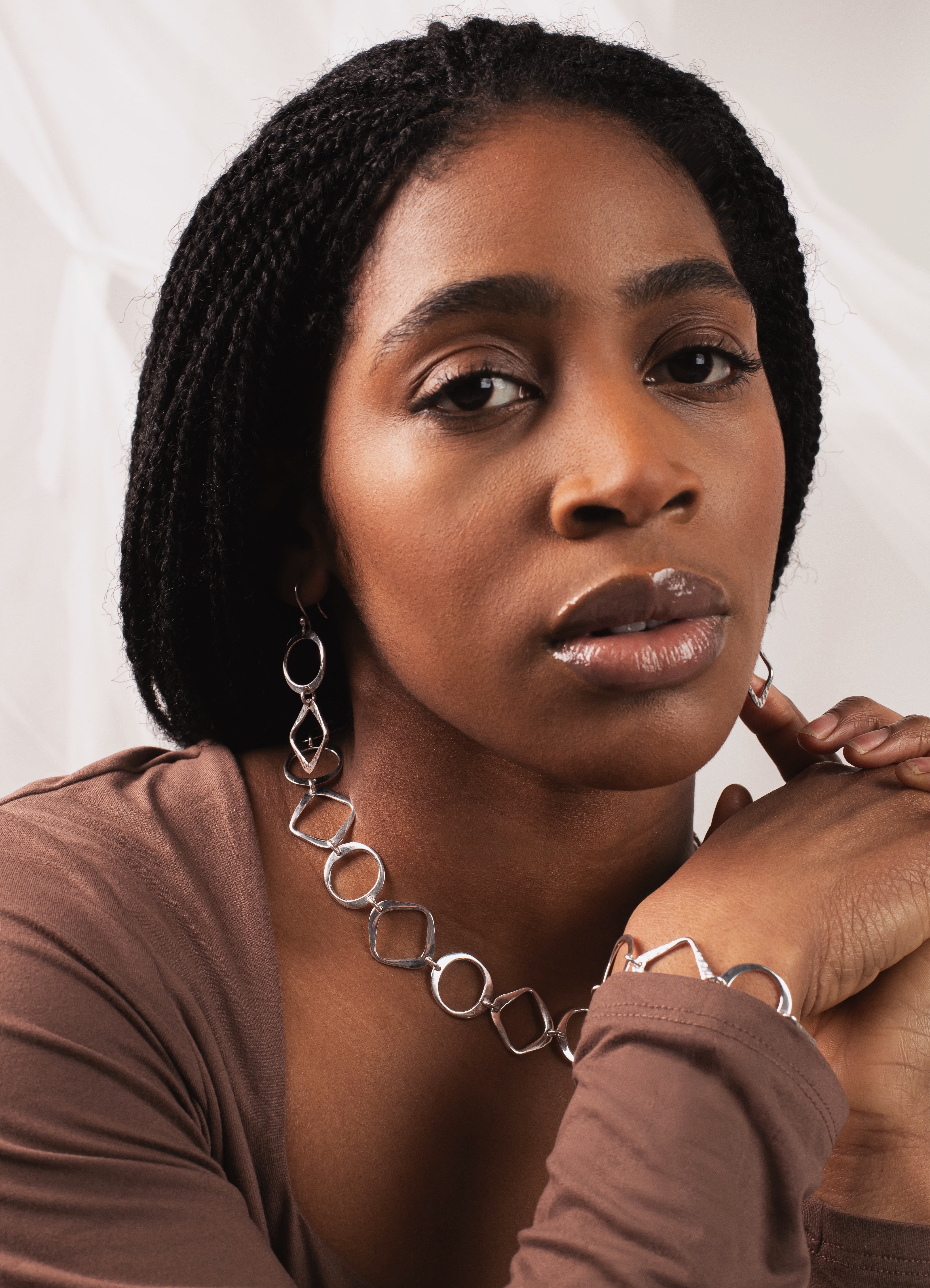 Woman wearing a brown top and silver jewelry against a white background