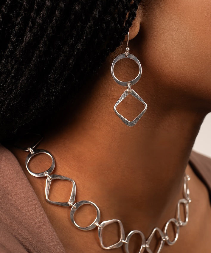 Silver necklace and earrings on a person wearing a black headscarf.
