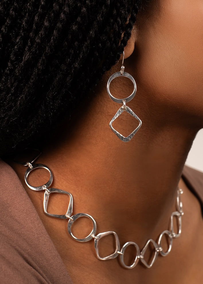 Silver necklace and earrings on a person wearing a black headscarf.