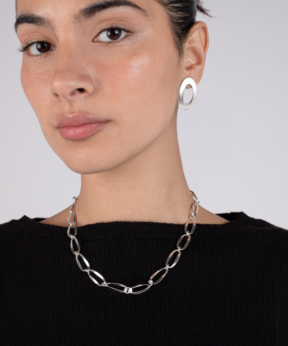 Woman wearing a silver chain necklace and hoop earrings against a plain background