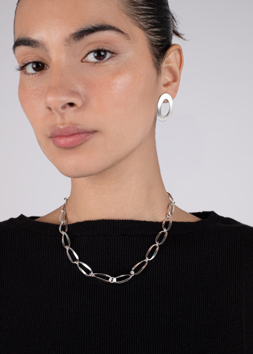 Woman wearing a silver chain necklace and hoop earrings against a plain background