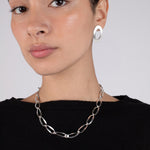 Woman wearing a silver chain necklace and hoop earrings against a plain background