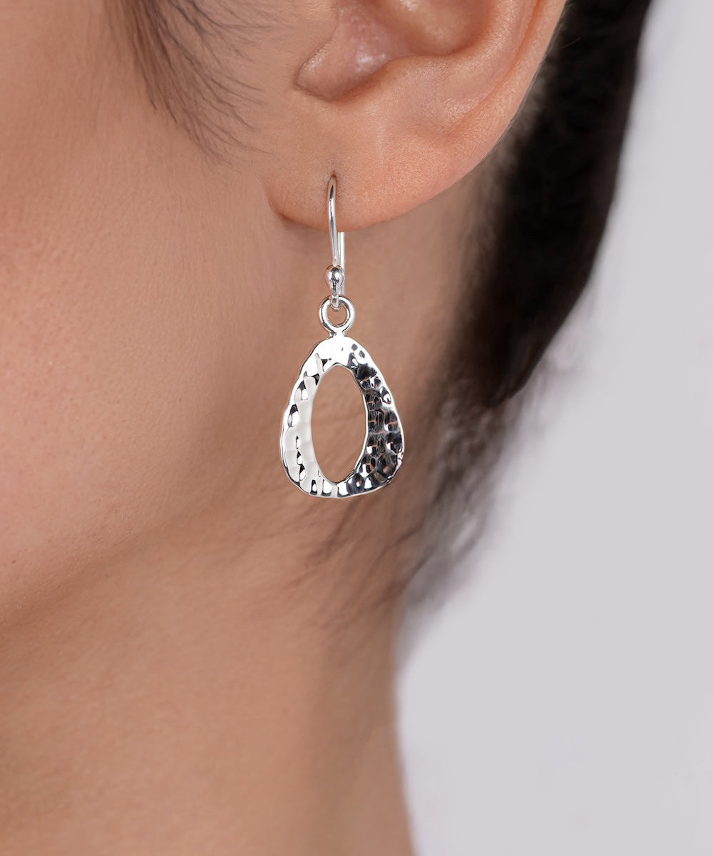 Silver teardrop earring worn by a person with a neutral background