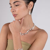 Woman wearing silver jewelry including a necklace, bracelet, and earrings on a plain background