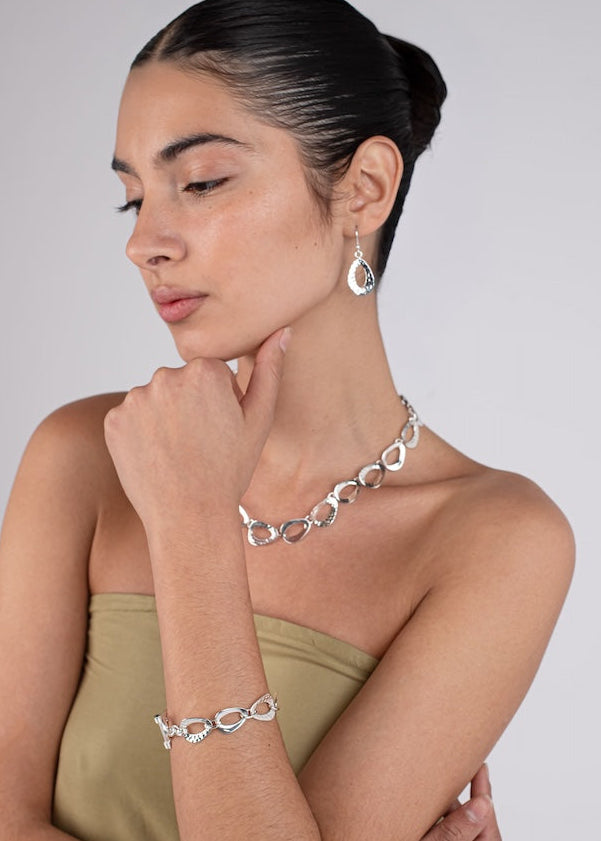 Woman wearing silver jewelry including a necklace, bracelet, and earrings on a plain background