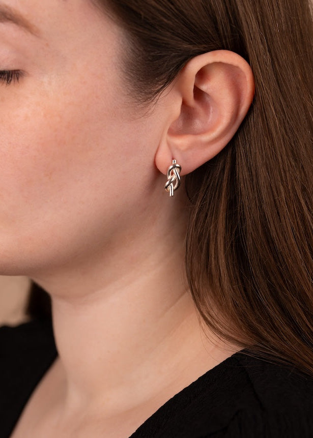 Close-up of a person wearing a silver earring with a leaf design.