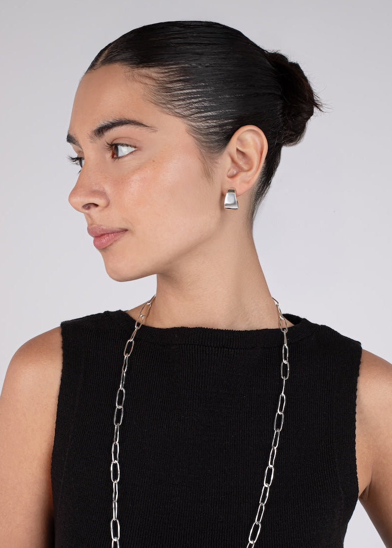 Woman wearing a long silver chain necklace and matching earrings on a plain background