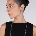 Woman wearing a long silver chain necklace and matching earrings on a plain background