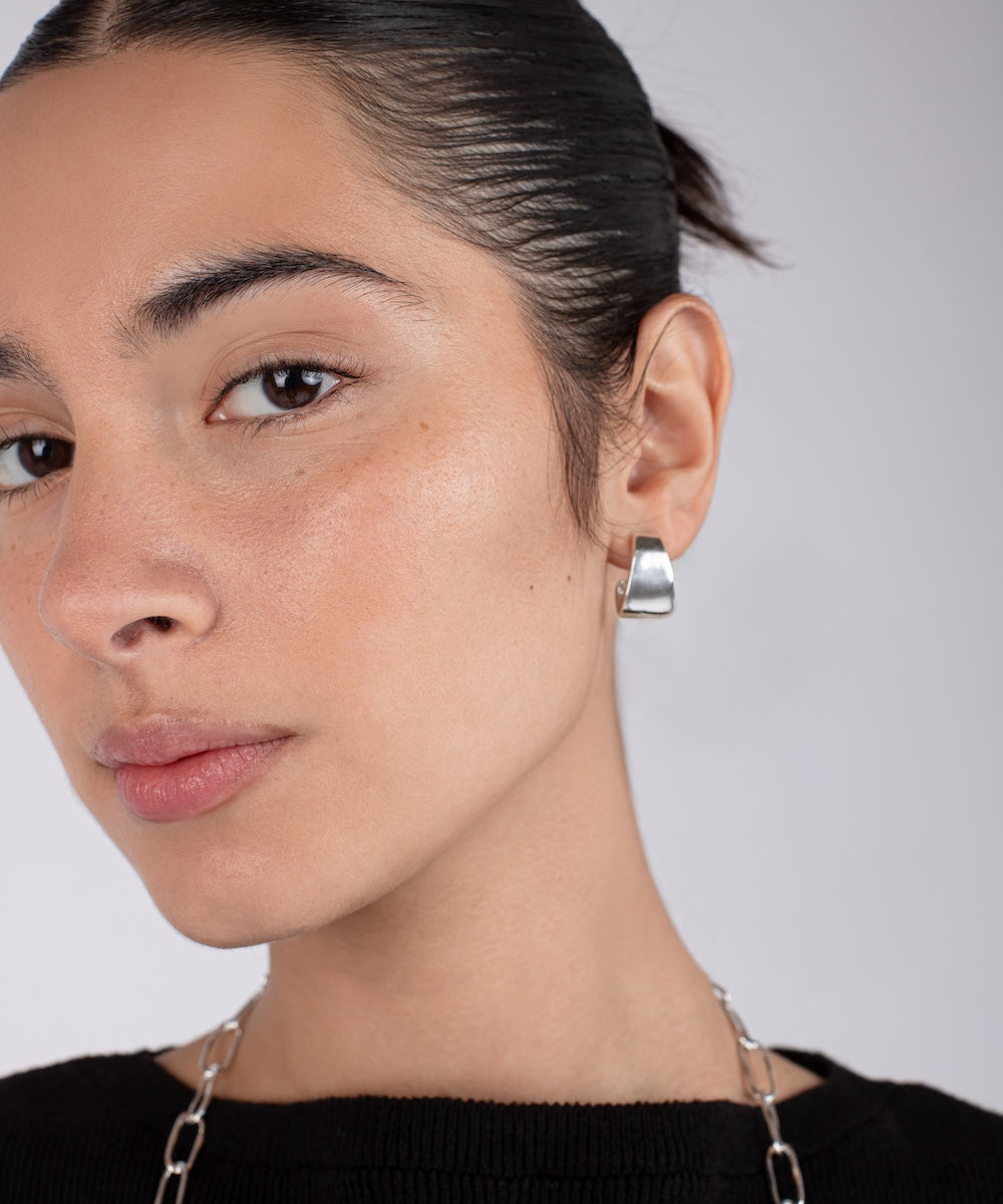 Close-up of a person wearing silver hoop earrings with a neutral background